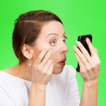 exhausted woman looking in a mirror isolated on green background